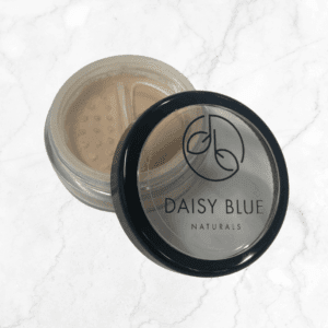 A partially open round container of Camellia Foundation with a black lid reveals light beige powder inside, displayed on a light marble surface.