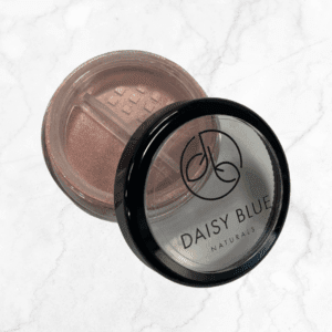 A round container of Flawless Glow Blush shimmery pink powder makeup features a clear, partially open lid with the logo and sits on a light marble surface.