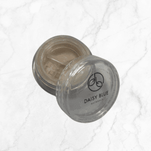 An open container of Flawless Glow Blush loose powder mineral makeup rests on a white marble surface, with its clear lid featuring the brand logo beside the soft beige blush inside.