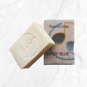A rectangular Purely Unscented Bar Soap with an embossed leaf design rests beside its box, labeled "Natural Soap" and "Daisy Blue Naturals," displayed on a white marble surface.