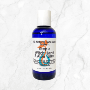 A blue bottle labeled "Witch Hazel & Aloe Toner" sits on white marble, highlighting its soothing formula with witch hazel and aloe—ideal for healing and refreshing all skin types.