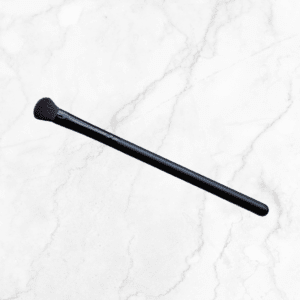 The Shadow Brush, featuring soft, angled bristles and a sleek black design, rests diagonally on a white marble surface.