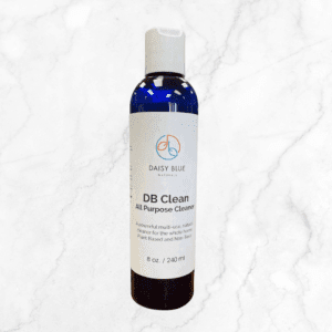 A blue plastic bottle of DB Clean Concentrated Cleaner 10x by Daisy Blue Naturals stands on a white marble surface, featuring a label that notes its plant-based, non-toxic formula and 8 oz (240 ml) size.