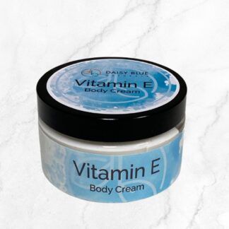 A small round container with a black lid labeled "Vitamin E Body Cream" sits on a light marble surface, its blue and white label emphasizing the moisturizing benefits of Vitamin E.