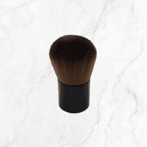 The Kabuki Brush, featuring a black handle and a round, fluffy head, stands upright on a white marble surface.