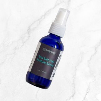 A blue spray bottle labeled "Sea Salt Texture Spray" rests on a white marble surface, showcasing this best-selling product that's perfect for achieving effortless, beachy hair texture.