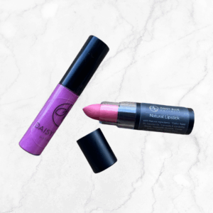 The Perfectly Pink & Wild Orchid Lipstick & Lip Gloss Duo by Daisy Blue, featuring a duo tube and open wild orchid lipstick with a black cap, is displayed on a light marble background.