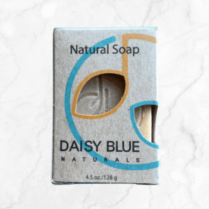 A box of Colloidal Oatmeal & Aloe Face Exfoliating Bar, showing part of the beige soap inside. The packaging features blue and yellow curved lines on a light gray background. The bar weighs 4.5 oz (128 g).