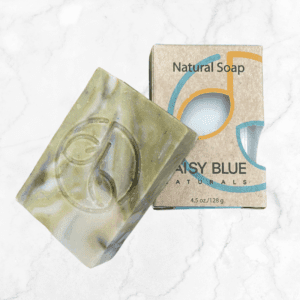 A green and purple marbled Sweetgrass & Lavender Body Bar Soap with a circular logo sits next to its brown box labeled "Natural Soap, Daisy Blue Naturals, 4.5 oz/128 g" on a white marble surface.